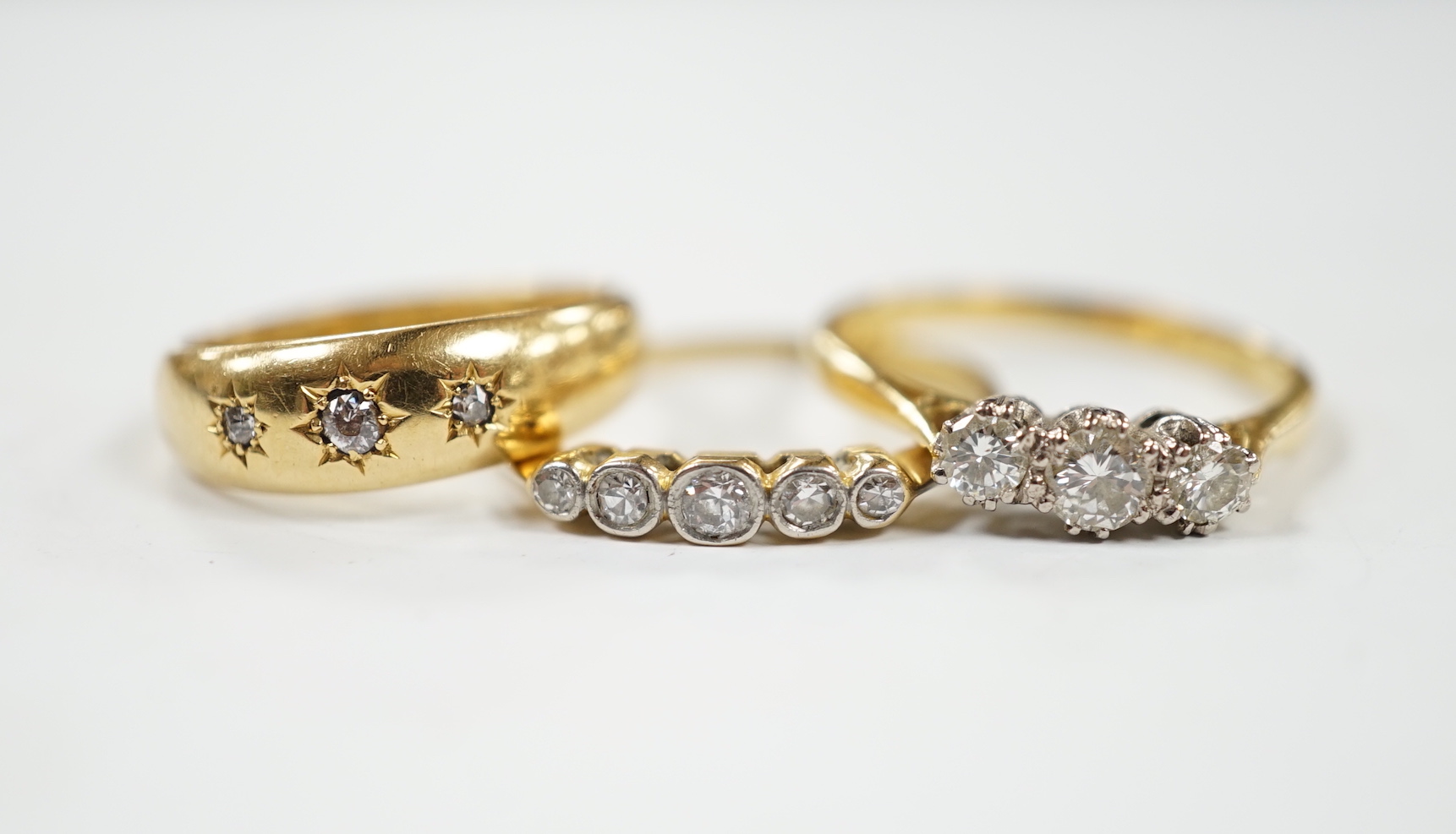 A late Victorian 18ct gold and gypsy set three stone diamond chip ring and two other 18ct and diamond set rings, three stone and five stone
